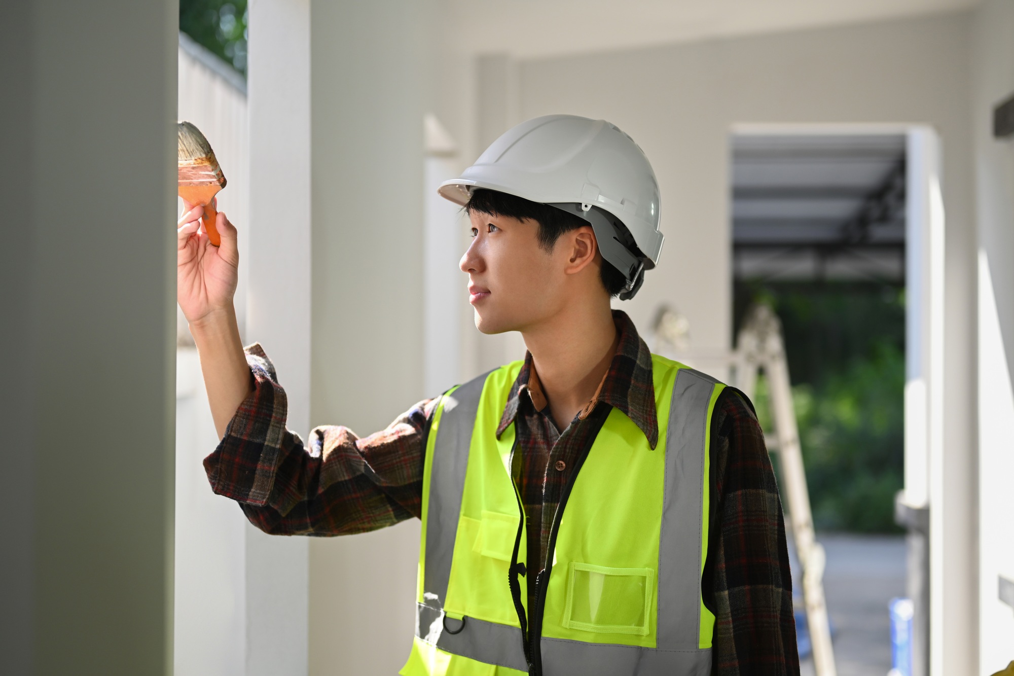 Asian male painter in safety helmet holding painting brush painting a white wall.